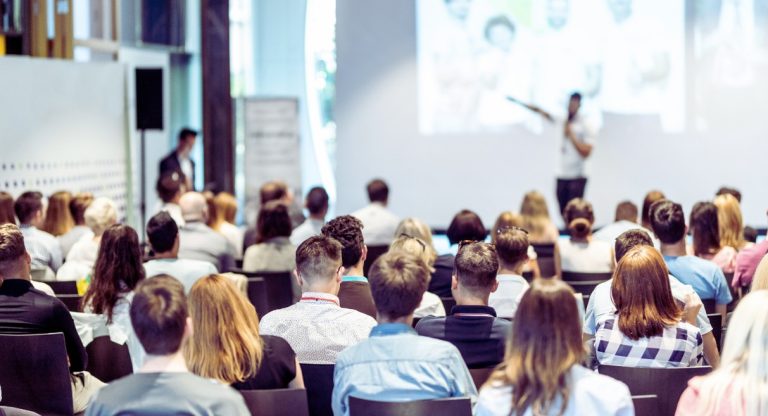 Salle de séminaire avec audience et conférencier devant grand écran