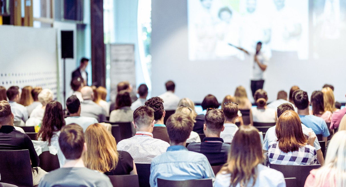 Salle de séminaire avec audience et conférencier devant grand écran