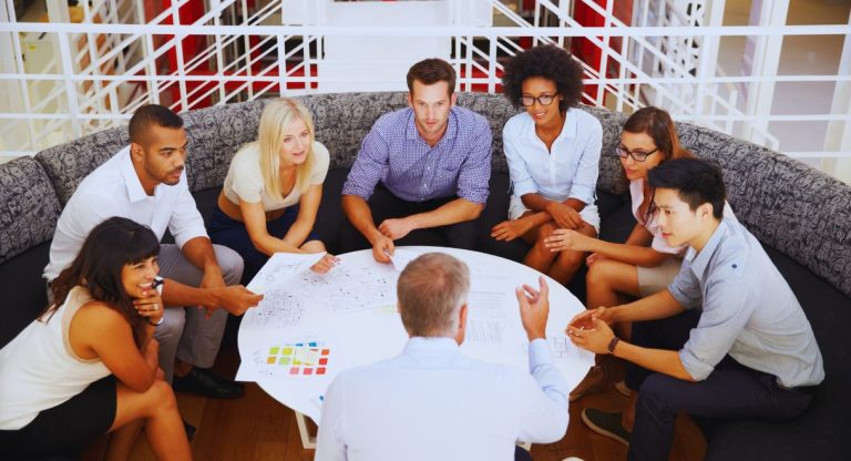 Groupe diversifié de collègues en discussion participative autour d'une table ronde