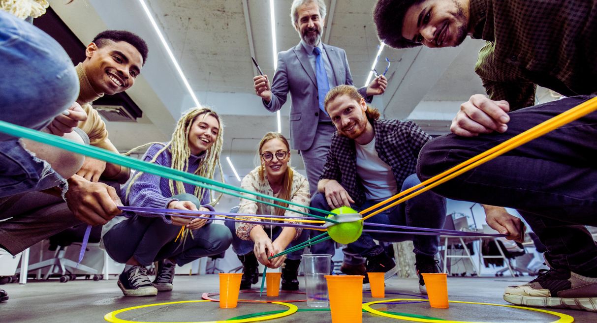 Équipe jouant à un jeu de team building avec des élastiques et des gobelets dans un bureau