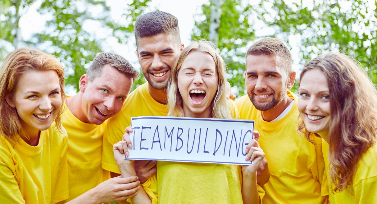 Groupe de collègues en t-shirts jaunes tenant une pancarte team building en plein air