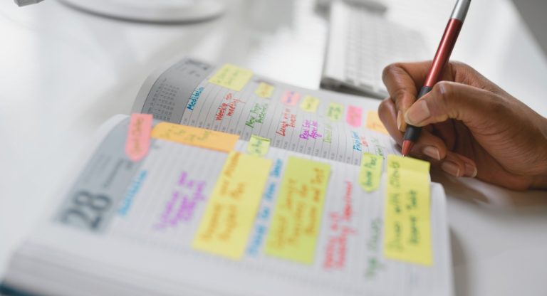 Main ecrivant un ordre du jour de reunion dans un agenda avec post-it colores